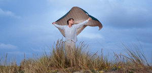 Ein Mann lässt am Strand eine Decke im Wind wehen und schaut dabei zur Seite